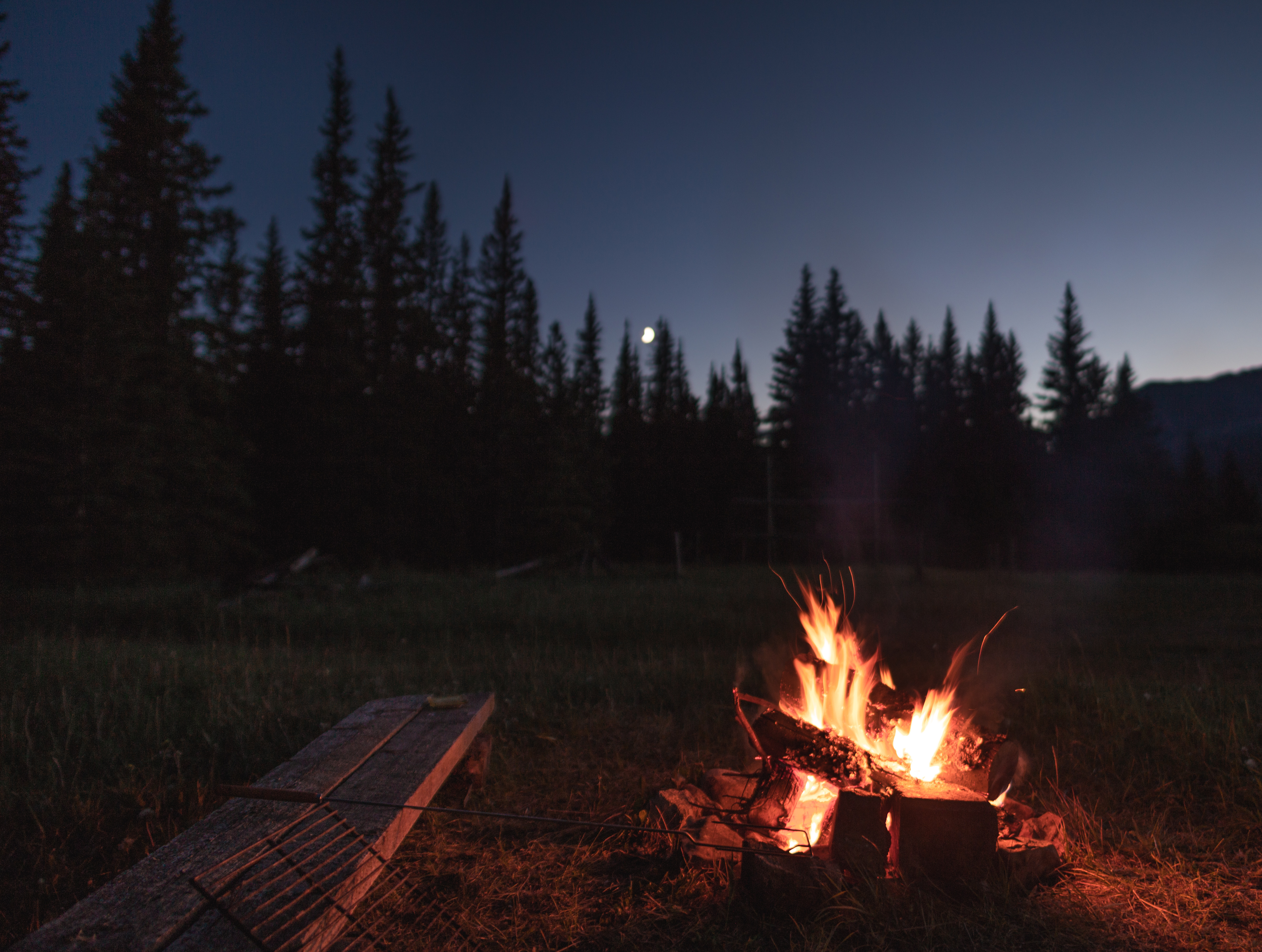 Campfire under the out of focus moon. There is a wooden bench beside